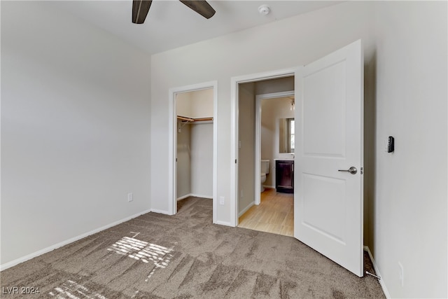 unfurnished bedroom featuring light carpet, a walk in closet, a closet, and ceiling fan