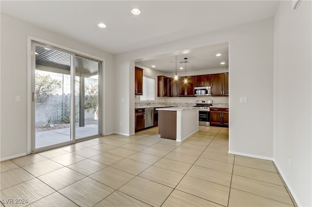 kitchen featuring hanging light fixtures, light stone counters, light tile patterned floors, stainless steel appliances, and a center island