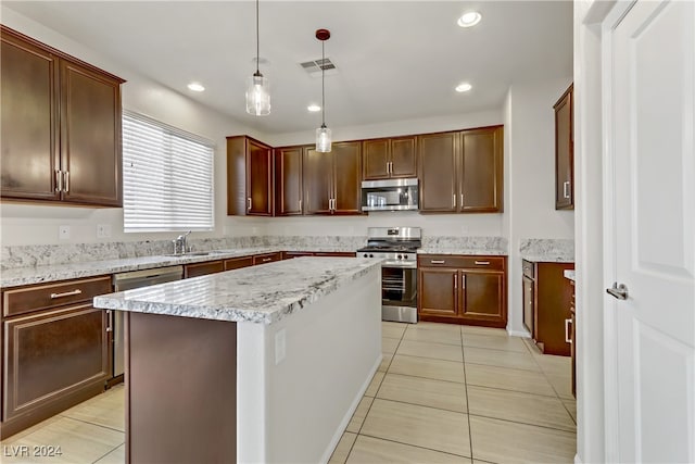 kitchen featuring a kitchen island, light stone countertops, light tile patterned flooring, pendant lighting, and appliances with stainless steel finishes