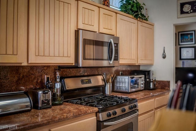 kitchen featuring light brown cabinetry, appliances with stainless steel finishes, and dark stone counters