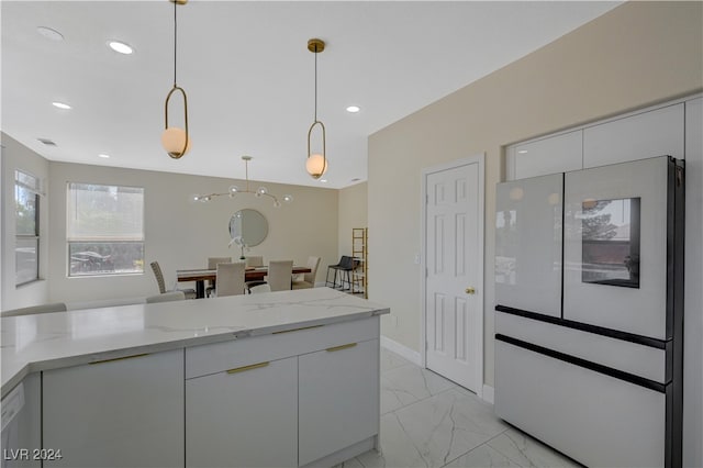 kitchen with light stone counters, white cabinetry, white fridge, and decorative light fixtures