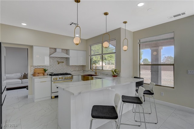 kitchen featuring a breakfast bar area, high end stainless steel range oven, white cabinetry, custom range hood, and decorative light fixtures