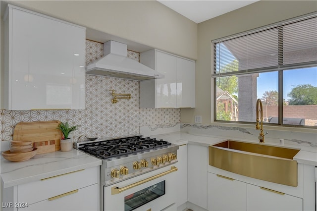 kitchen featuring wall chimney range hood, high end white range, sink, white cabinetry, and light stone counters