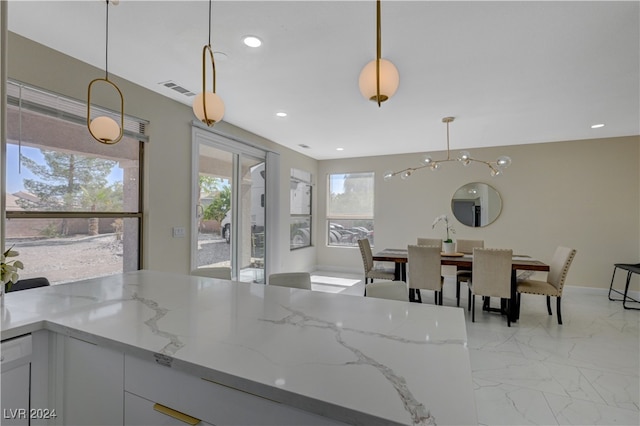 kitchen with white cabinets, light stone countertops, a chandelier, and hanging light fixtures