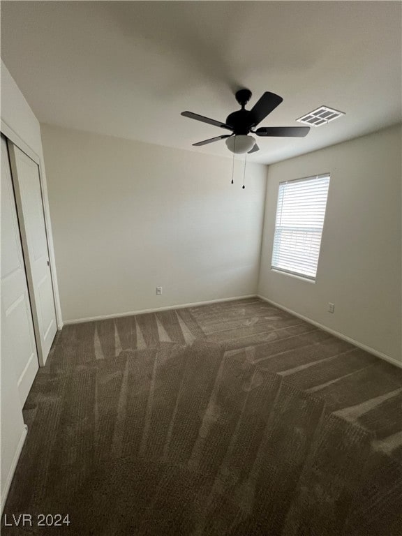 unfurnished bedroom featuring a closet, ceiling fan, and dark colored carpet