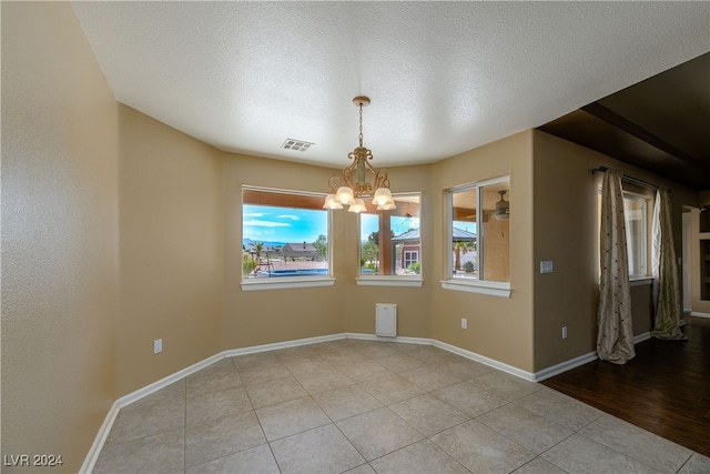 unfurnished dining area featuring light tile patterned floors, a textured ceiling, and an inviting chandelier