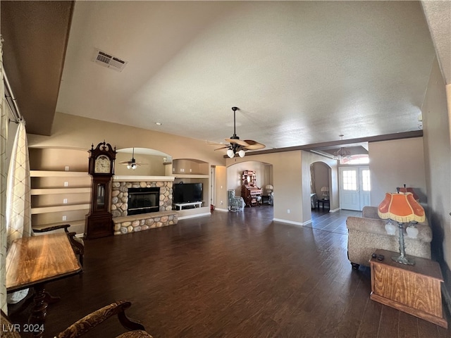 living room with built in shelves, a textured ceiling, dark hardwood / wood-style floors, ceiling fan, and a fireplace