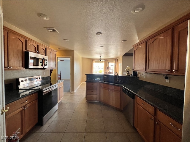 kitchen with appliances with stainless steel finishes, sink, dark stone counters, kitchen peninsula, and tile patterned floors