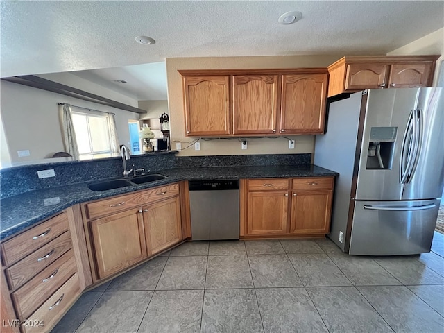 kitchen with sink, a textured ceiling, light tile patterned floors, appliances with stainless steel finishes, and dark stone counters