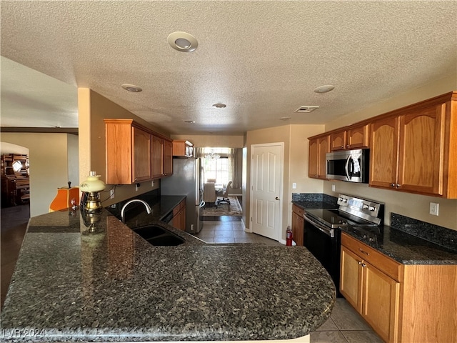 kitchen with sink, light tile patterned floors, kitchen peninsula, stainless steel appliances, and a textured ceiling