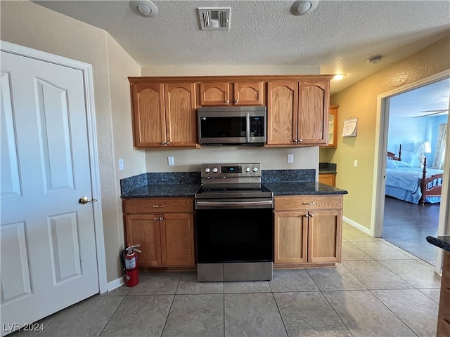 kitchen featuring stainless steel appliances, light tile patterned floors, and dark stone counters