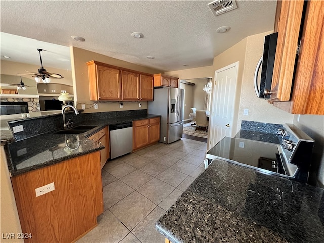 kitchen with light tile patterned flooring, sink, a textured ceiling, appliances with stainless steel finishes, and dark stone counters