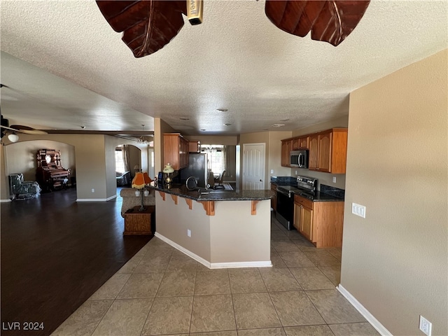 kitchen with a breakfast bar, a textured ceiling, appliances with stainless steel finishes, kitchen peninsula, and ceiling fan