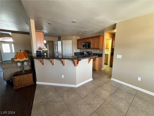 kitchen with a breakfast bar area, kitchen peninsula, a textured ceiling, and appliances with stainless steel finishes