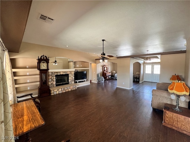 living room with a stone fireplace, a textured ceiling, dark hardwood / wood-style floors, built in features, and ceiling fan