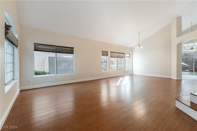 empty room with dark wood-type flooring, vaulted ceiling, a notable chandelier, and a wealth of natural light