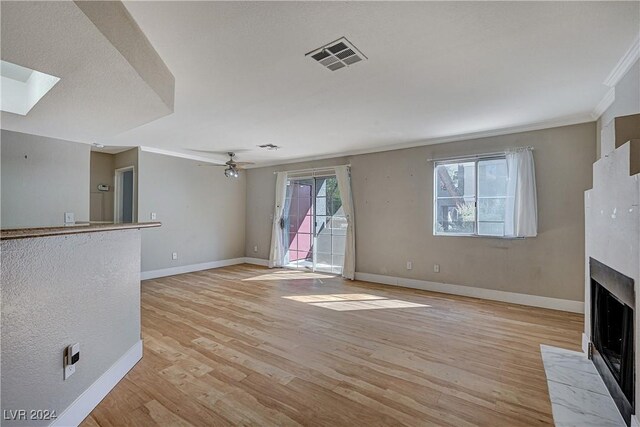 unfurnished living room featuring ceiling fan, light hardwood / wood-style floors, ornamental molding, and a skylight