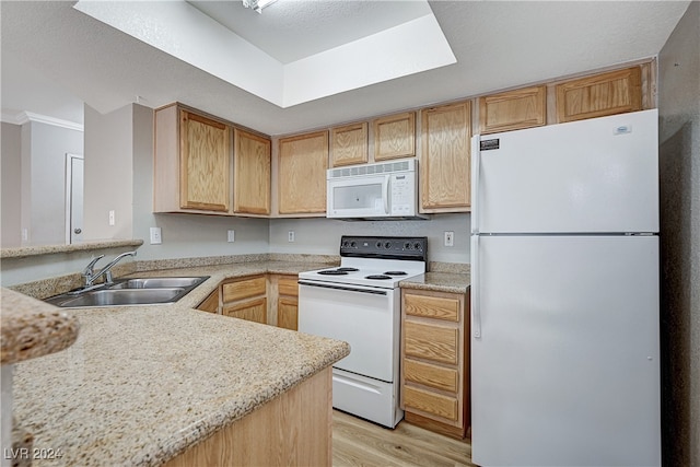 kitchen with light wood finished floors, light countertops, a sink, white appliances, and a peninsula