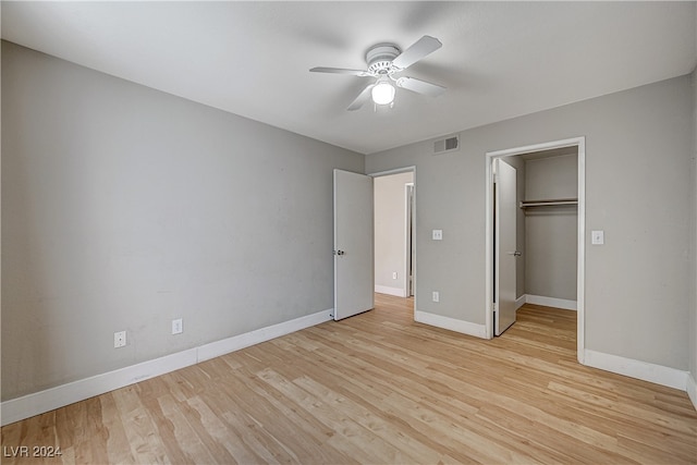 unfurnished bedroom with a walk in closet, visible vents, light wood-style flooring, a ceiling fan, and baseboards