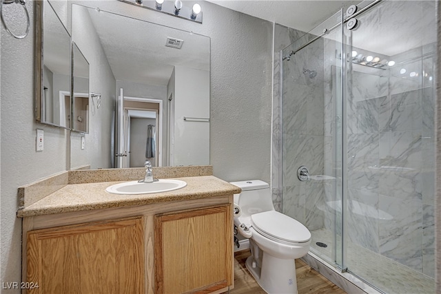 full bathroom with a marble finish shower, a textured wall, toilet, wood finished floors, and vanity