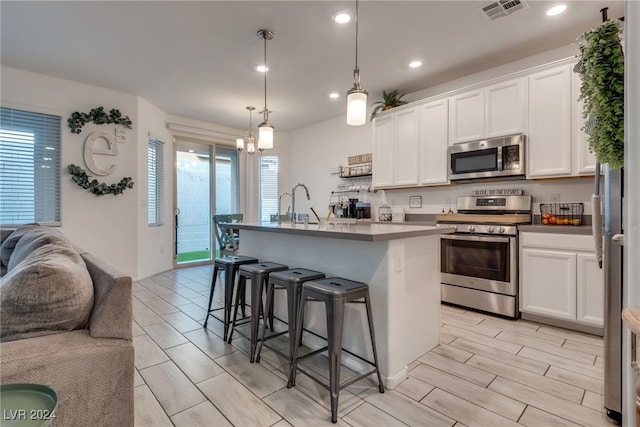 kitchen featuring white cabinetry, stainless steel appliances, and an island with sink