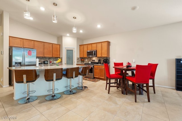 kitchen featuring stainless steel appliances, hanging light fixtures, an island with sink, and decorative backsplash