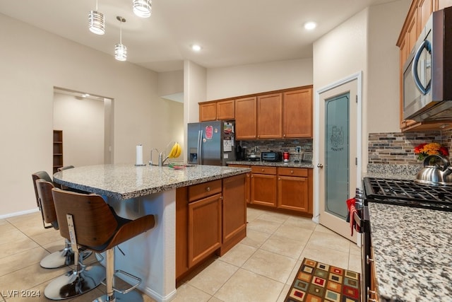 kitchen featuring an island with sink, light stone counters, stainless steel appliances, a breakfast bar, and pendant lighting