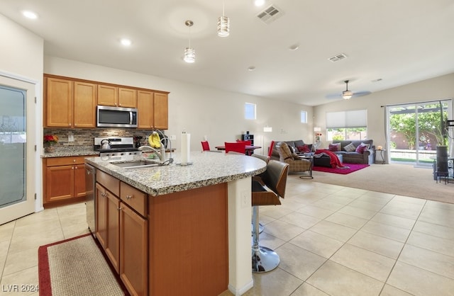 kitchen featuring light stone counters, an island with sink, hanging light fixtures, sink, and appliances with stainless steel finishes