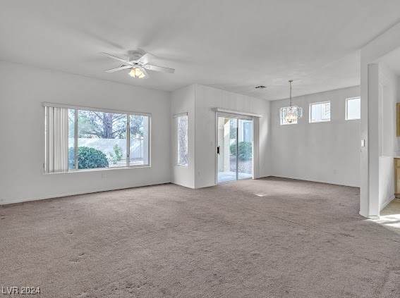 unfurnished living room featuring light carpet, ceiling fan with notable chandelier, and a healthy amount of sunlight