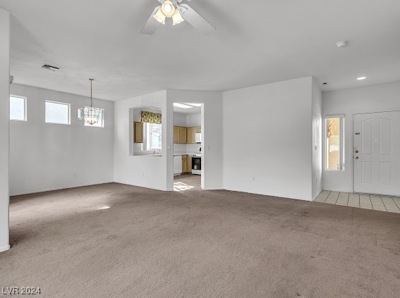 unfurnished living room with light carpet, ceiling fan with notable chandelier, and a healthy amount of sunlight