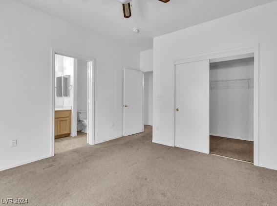 unfurnished bedroom with ceiling fan, a closet, light colored carpet, and ensuite bath