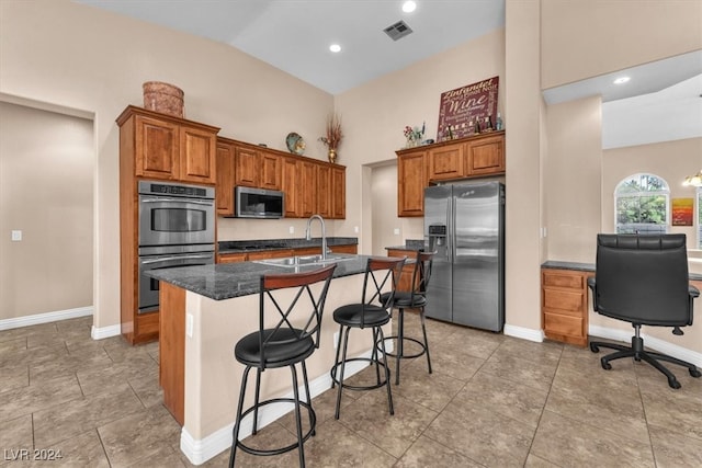 kitchen with sink, a kitchen island with sink, stainless steel appliances, dark stone countertops, and a breakfast bar area