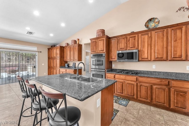 kitchen featuring vaulted ceiling, sink, an island with sink, appliances with stainless steel finishes, and a kitchen bar