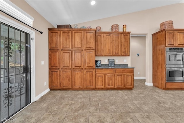 kitchen featuring double oven, lofted ceiling, dark stone countertops, and light tile patterned floors