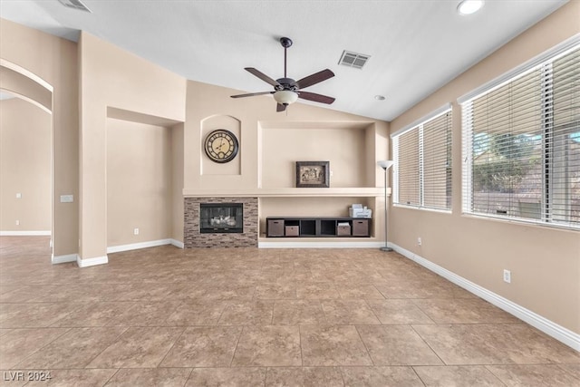 unfurnished living room featuring lofted ceiling, ceiling fan, light tile patterned floors, and a stone fireplace