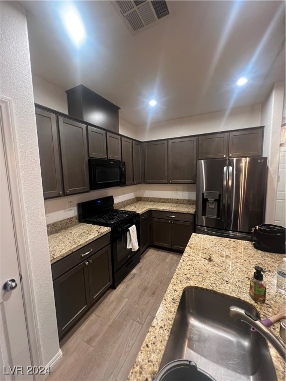 kitchen with black appliances, light stone countertops, sink, and light hardwood / wood-style flooring