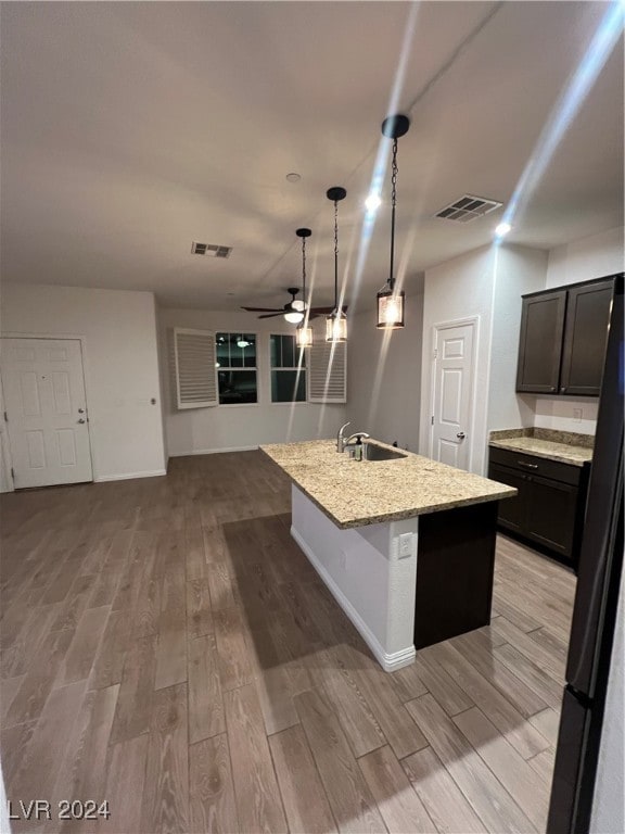 kitchen with an island with sink, sink, light wood-type flooring, and light stone counters