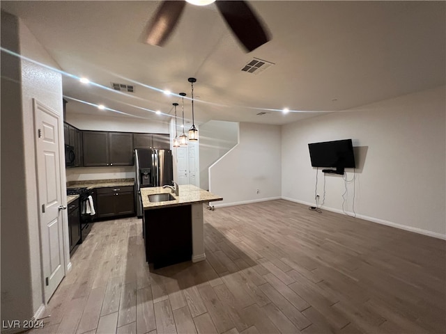 kitchen with decorative light fixtures, a center island with sink, light wood-type flooring, and black gas range oven