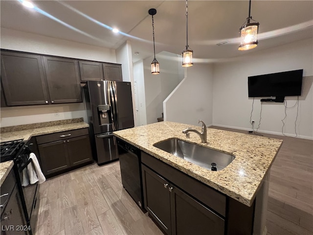 kitchen with pendant lighting, light hardwood / wood-style flooring, a center island with sink, sink, and black appliances