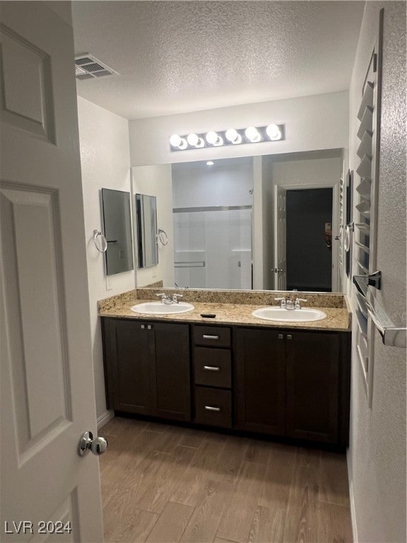 bathroom with hardwood / wood-style floors, a shower with door, vanity, and a textured ceiling