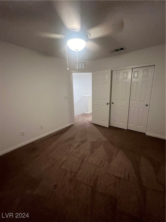 unfurnished bedroom with ceiling fan, a textured ceiling, a closet, and dark colored carpet