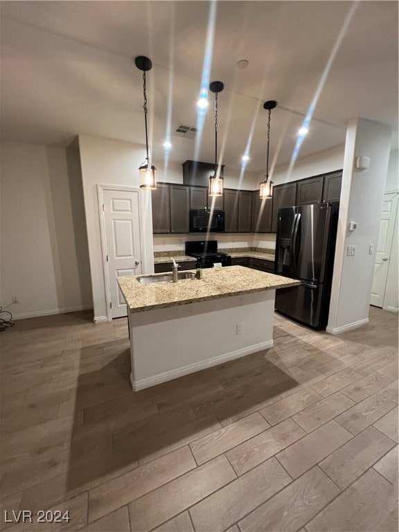 kitchen with light stone counters, light wood-type flooring, black appliances, and hanging light fixtures