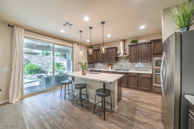 kitchen featuring hardwood / wood-style flooring, wall chimney range hood, hanging light fixtures, and stainless steel appliances