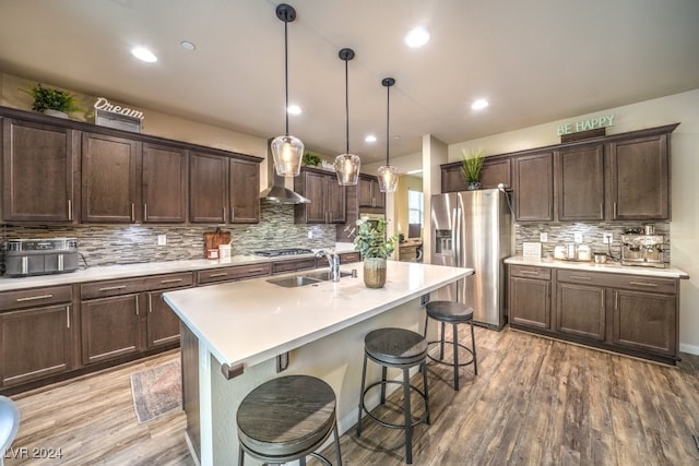 kitchen with a center island with sink, hanging light fixtures, stainless steel appliances, and light hardwood / wood-style flooring