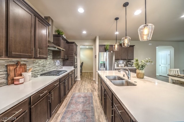 kitchen with pendant lighting, sink, backsplash, wall chimney range hood, and appliances with stainless steel finishes