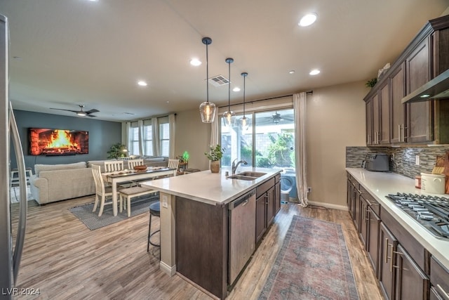 kitchen with light hardwood / wood-style floors, decorative light fixtures, sink, an island with sink, and appliances with stainless steel finishes