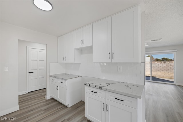 kitchen featuring backsplash, a textured ceiling, white cabinetry, light stone counters, and light hardwood / wood-style flooring