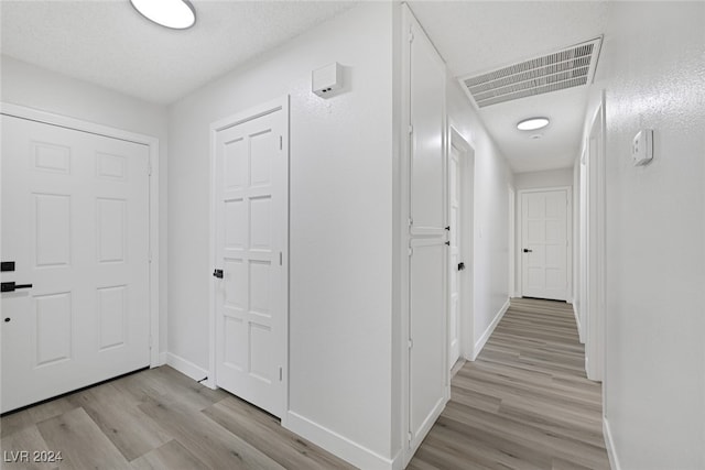 hallway with light hardwood / wood-style floors and a textured ceiling