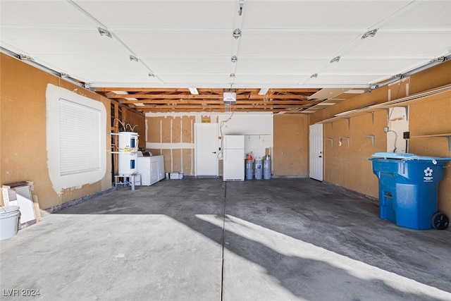 garage featuring water heater, washing machine and dryer, and white refrigerator