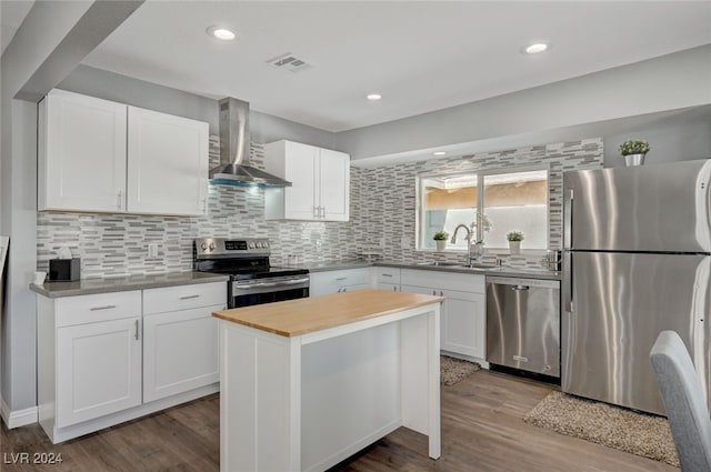 kitchen with sink, wall chimney range hood, a kitchen island, stainless steel appliances, and white cabinets